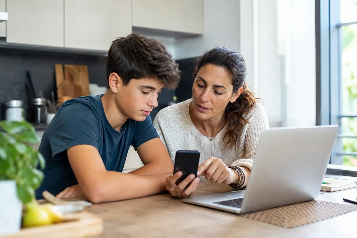Genitore e adolescente che parlano di sicurezza online con smartphone e laptop in casa